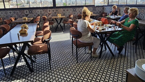A rooftop dining area with tables and chairs, large windows offering city views, and patterned flooring. - Rever Hotel (Sanliurfa)
