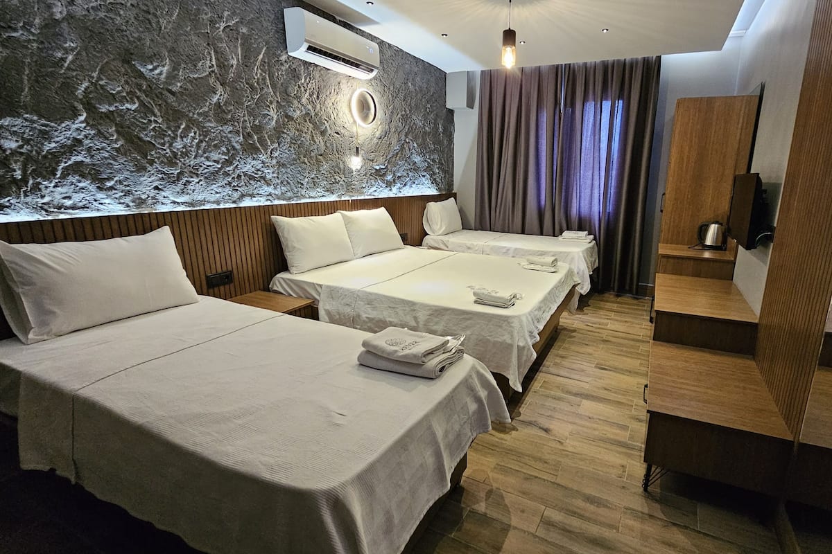 Une chambre d’hôtel avec deux lits, un plancher en bois, un climatiseur fixé au mur et un miroir qui reflète la pièce.