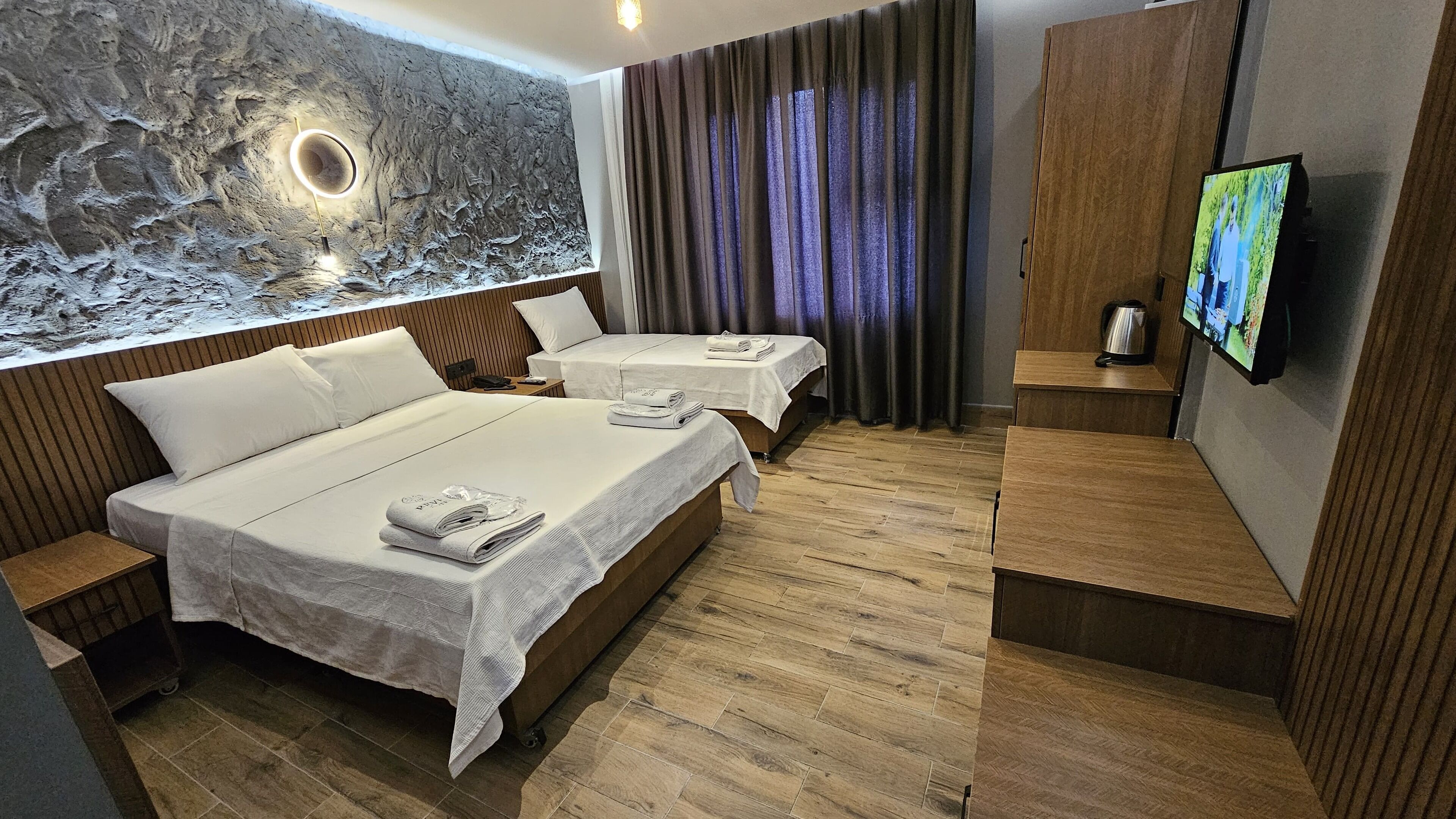 A hotel room with two beds, a stone wall, a television, and a wooden floor.