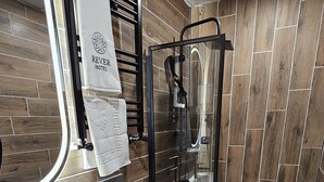 A bathroom with a wooden floor, a white sink, a toilet, and a glass-enclosed shower. - Rever Hotel (Sanliurfa)