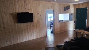 Ein Zimmer mit Holzwänden, einem an der Wand befestigten Flachbildfernseher, einem Holztisch und einer Tür.