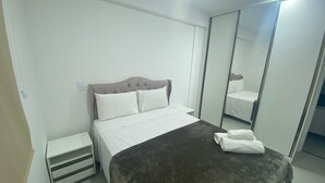 Hotellihuone, jossa on sänky, yöpöytä, peili ja vaatekaappi.