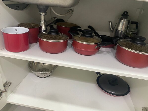 A kitchen shelf with various red cookware items, including pots and pans, and a colander.