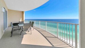 A balcony with a table and chairs, overlooking a beach with clear turquoise water and a view of the ocean. - Ocean Villa 2004 (Panama City Beach)