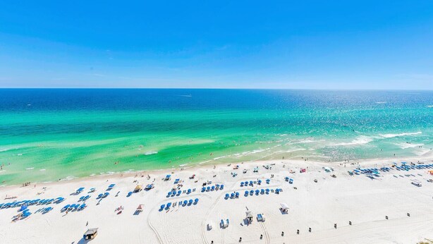 A beach with rows of blue beach chairs and umbrellas, a sandy shore, and the ocean in the background. - Ocean Villa 2004 (Panama City Beach)