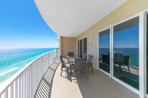 Un balcón con puerta de cristal, mesa y sillas, con vista a la playa y al océano.