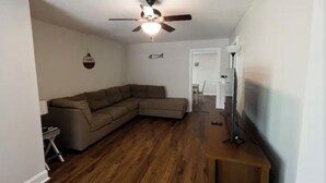 Ein Wohnzimmer mit einer Eckcouch, einem Deckenventilator und Holzboden.