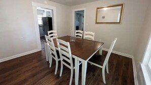 Ein Esszimmer mit Holztisch und weißen Stühlen, einem gerahmten Bild an der Wand und einer Tür, die in einen anderen Raum führt.