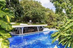 Una estructura flotante con techo sobre una piscina, rodeada de abundante vegetación.