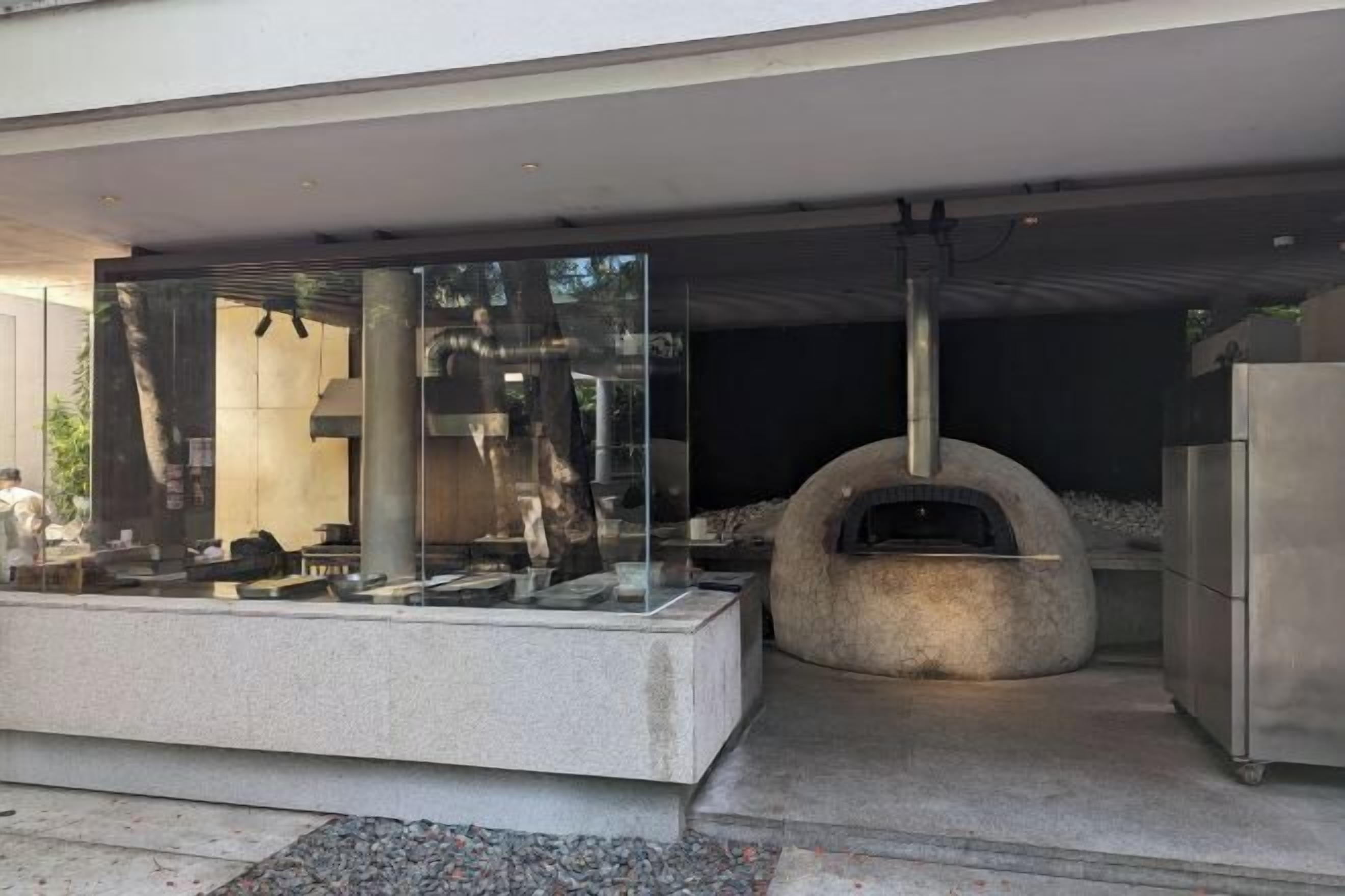 An outdoor kitchen area with a stone oven, a glass enclosure with kitchenware, and a modern building facade.