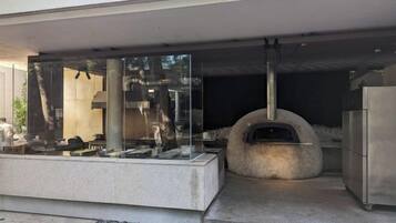 An outdoor kitchen area with a stone oven, a glass enclosure with kitchenware, and a modern building facade.