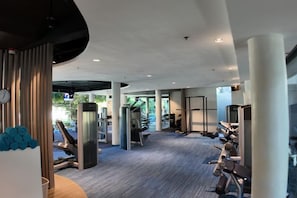 Un gimnasio con diversos equipos de ejercicio, incluyendo cintas de correr y máquinas de pesas, bajo un techo alto con luz natural.