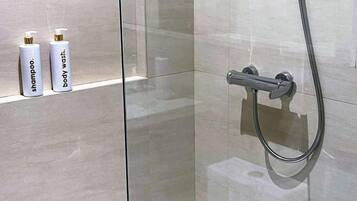 A bathroom with a glass shower enclosure, a handheld showerhead, and two bottles of shampoo and body wash on a shelf.