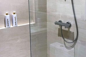 A bathroom with a glass shower enclosure, a handheld showerhead, and two bottles of shampoo and body wash on a shelf. - Studio for 5 at Tambuli Residences Garden View by Dominik Studio with Pool & Balcony in Mactan (Lapu-Lapu City)