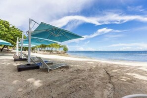 Una playa con tumbonas y sombrillas, cielo despejado y vista al océano.