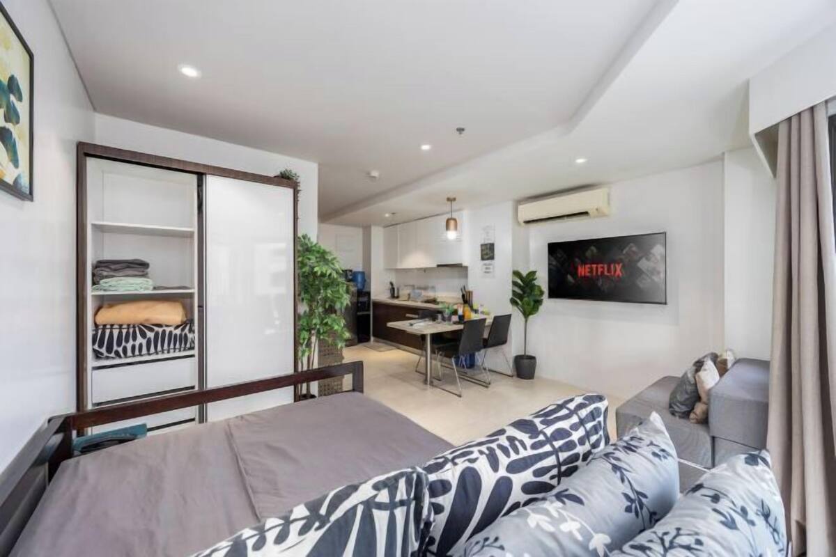 Una habitación de hotel moderna con cama, sofá, kitchenette, zona de comedor y un televisor mostrando el logo de Netflix.