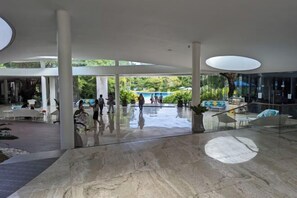 A spacious lobby with a marble floor, large windows, and a view of an outdoor swimming pool. - Studio for 5 at Tambuli Residences Garden View by Dominik Studio with Pool & Balcony in Mactan (Lapu-Lapu City)