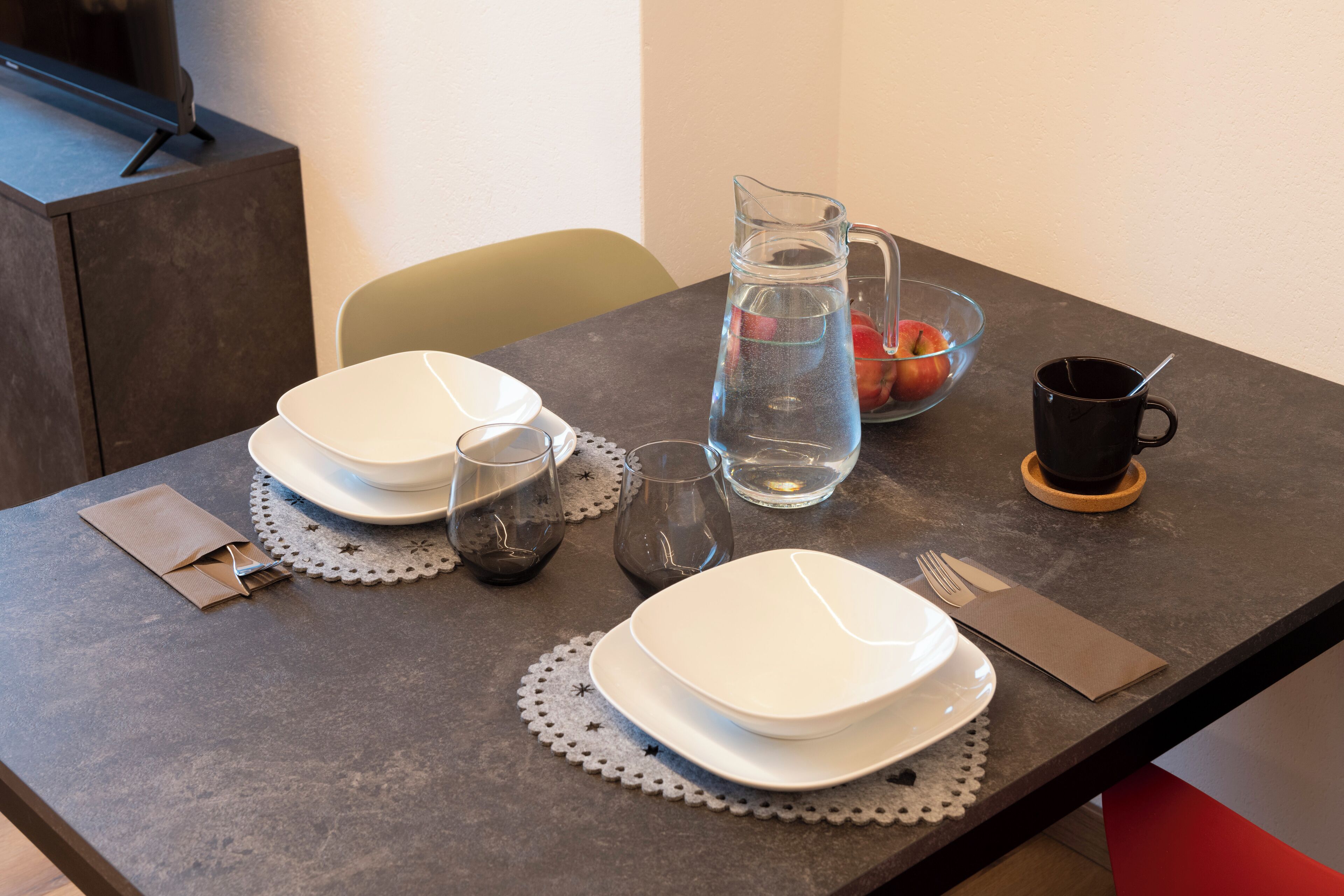 Ett matbord dukat med tallrikar, glas, en kanna och en skål med frukt.
