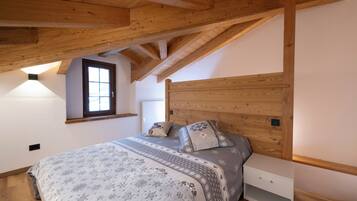 A bedroom with a wooden ceiling, a bed with patterned bedding, a nightstand, and a window.