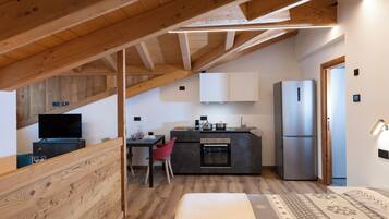 Cocina compacta con vigas de madera, un refrigerador y una zona de comedor con una silla roja.