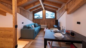 Una habitación acogedora con techo de madera, un sofá, una mesa de comedor con platos y una jarra, y vistas al exterior a través de grandes ventanales.