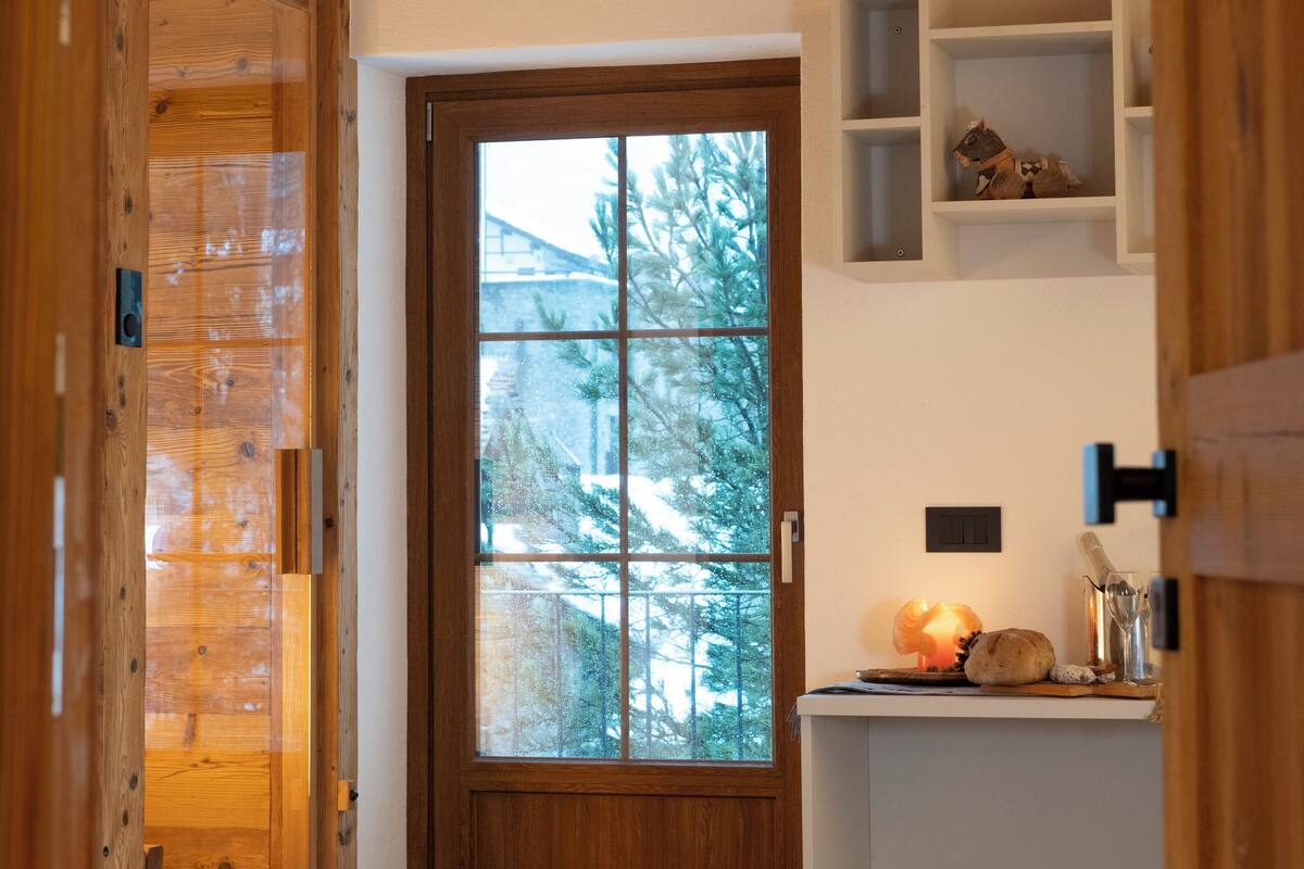 A wooden interior with a door leading to a room, a small wooden stool, and a shelf with items.