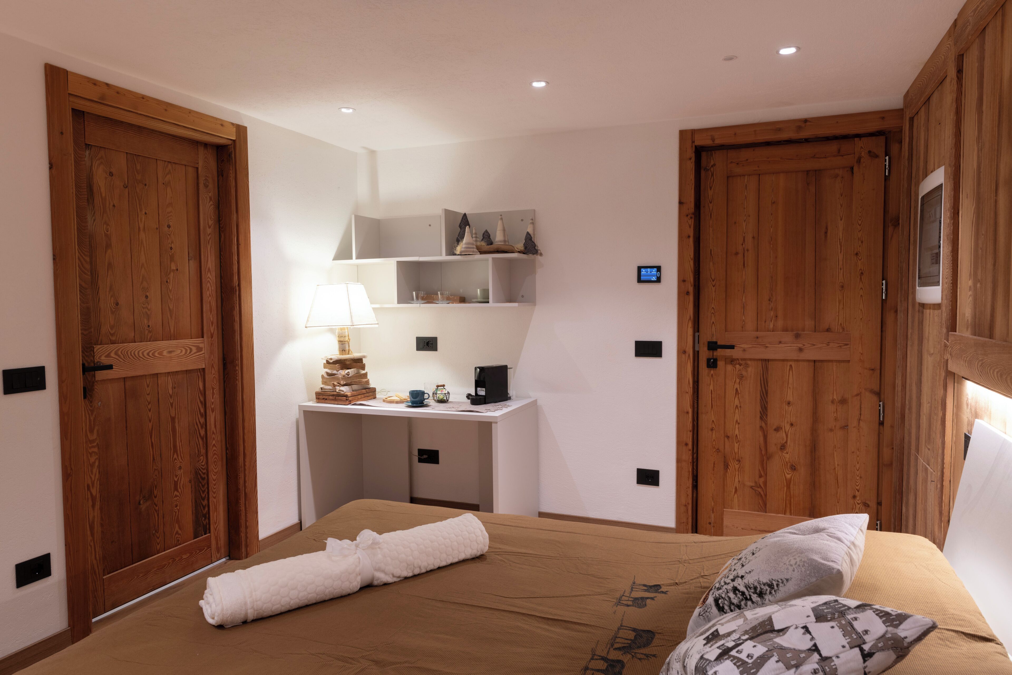 A bedroom with a bed, a desk, and two wooden doors.