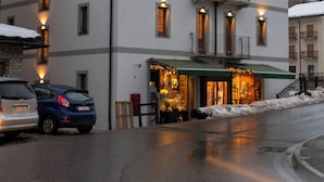 Un hotel de varios pisos con balcones, una tienda en la planta baja y coches aparcados.