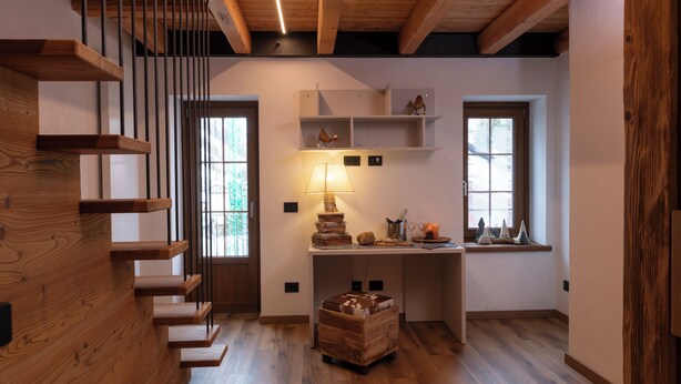 Un interior moderno con una escalera de madera, un escritorio con lámpara y estantes con objetos decorativos.