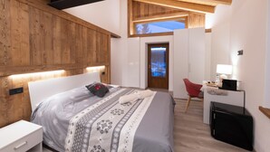 Un dormitorio moderno con techo de madera, cama con ropa de cama estampada, escritorio con lámpara y una silla roja.