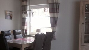 Un comedor con una mesa de madera y seis sillas, una ventana con cortinas, y un aparador con puertas de vidrio.