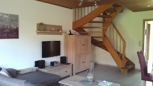 Una sala de estar con sofá, televisión, mueble de madera y una escalera.