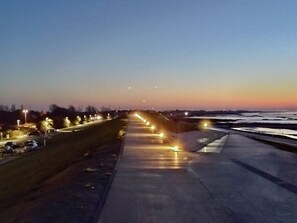 Une longue route droite, bordée de lampadaires et de voitures garées.