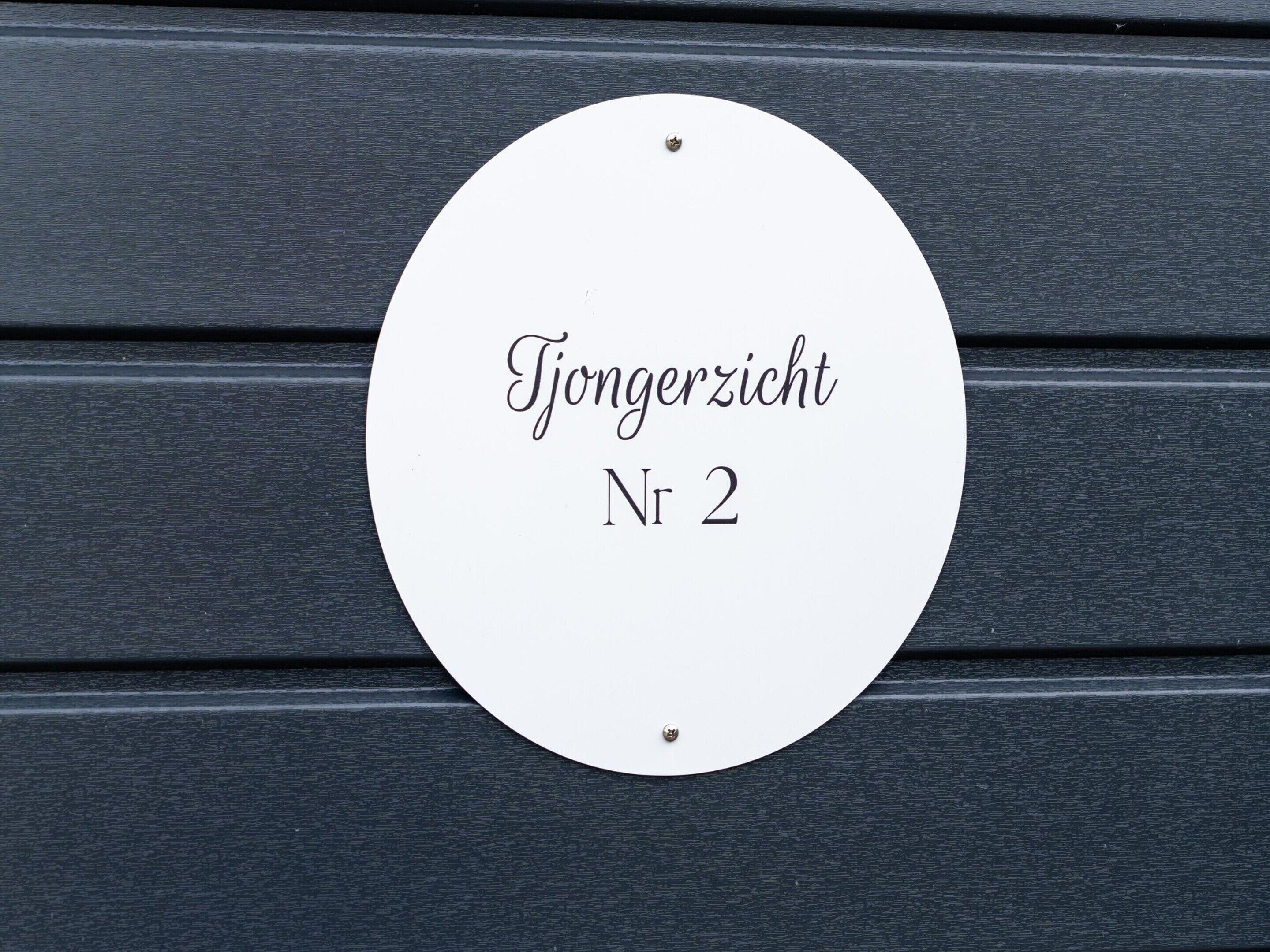 A white circular sign with the text "Tjongerzicht Nr 2" on a dark wooden background.