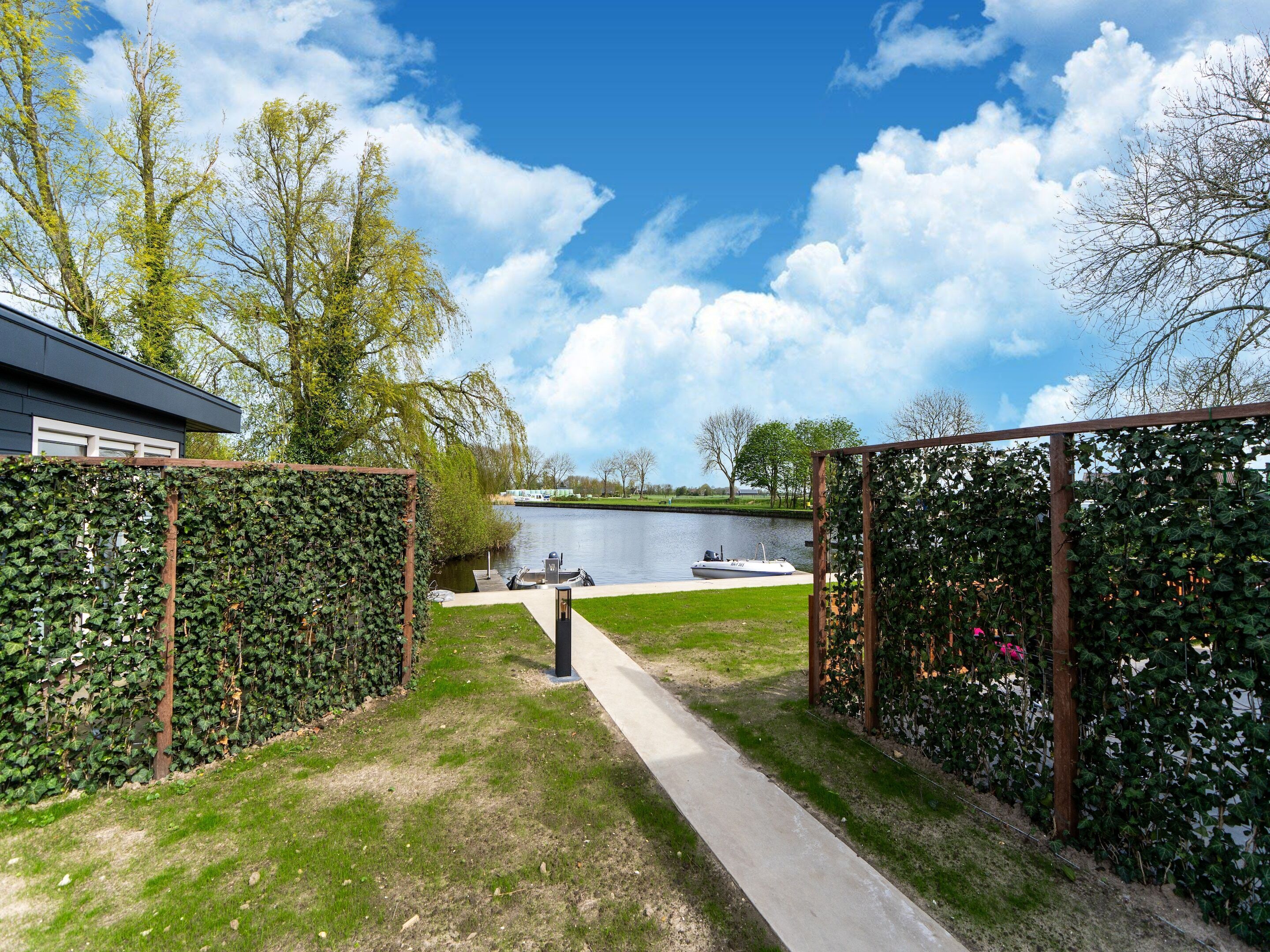A pathway leading to a body of water, surrounded by greenery and a building.