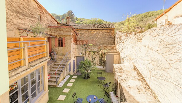 Un patio con pared de piedra, cerca de madera, un pequeño jardín y una mesa con sillas.