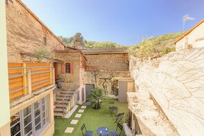 Um pátio com muro de pedra, cerca de madeira, um pequeno jardim e uma mesa com cadeiras.