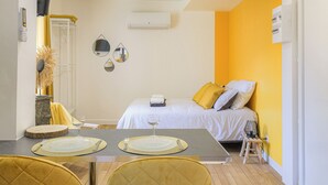 Habitación de hotel con cama, una mesa de comedor con platos y cubiertos, un taburete pequeño y un espejo en la pared.