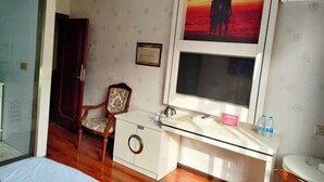 Habitación de hotel con cama, escritorio con espejo, una silla, un cuadro enmarco y un inodoro.