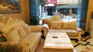 Una habitación con un sofá grande y ornamentado, un sillón a juego, una mesita y un ventanal con vistas a una calle y tiendas.