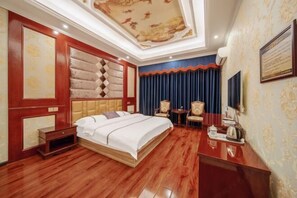 A hotel room with a large bed, a desk, a chair, a small table, and a television. - Meishan Xingchen Hotel (Meishan)