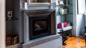 A room with a fireplace, a framed floral painting above it, and a bookshelf with books and decorative items. - Douro D'heart - Casa Familiar no Centro da Régua (Peso da Régua)