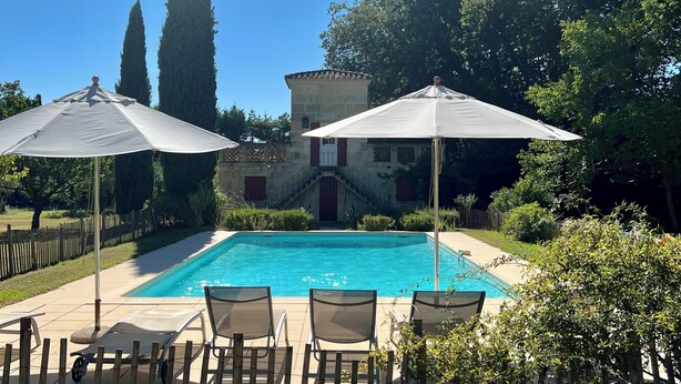 Una piscina amb dues ombrel·les, envoltada de cadires, i un edifici amb una escala al fons.