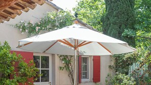 Terrassa exterior amb taula preparada per dinar, envoltada de cadires i una ombria que proporciona protecció del sol.