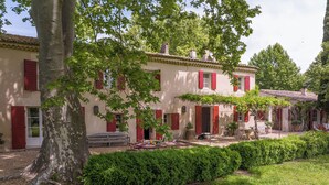 Un edifici amb persianes vermelles, un jardí amb una banca i un arbre al primer pla.