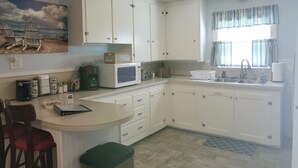 Cocina pequeña con armarios blancos, un microondas, un lavamanos y un ventanal con cortinas.