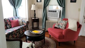Una sala de estar con un sofá floral, un sillón rojo, una mesita redonda con revistas, una lámpara y un radiador.