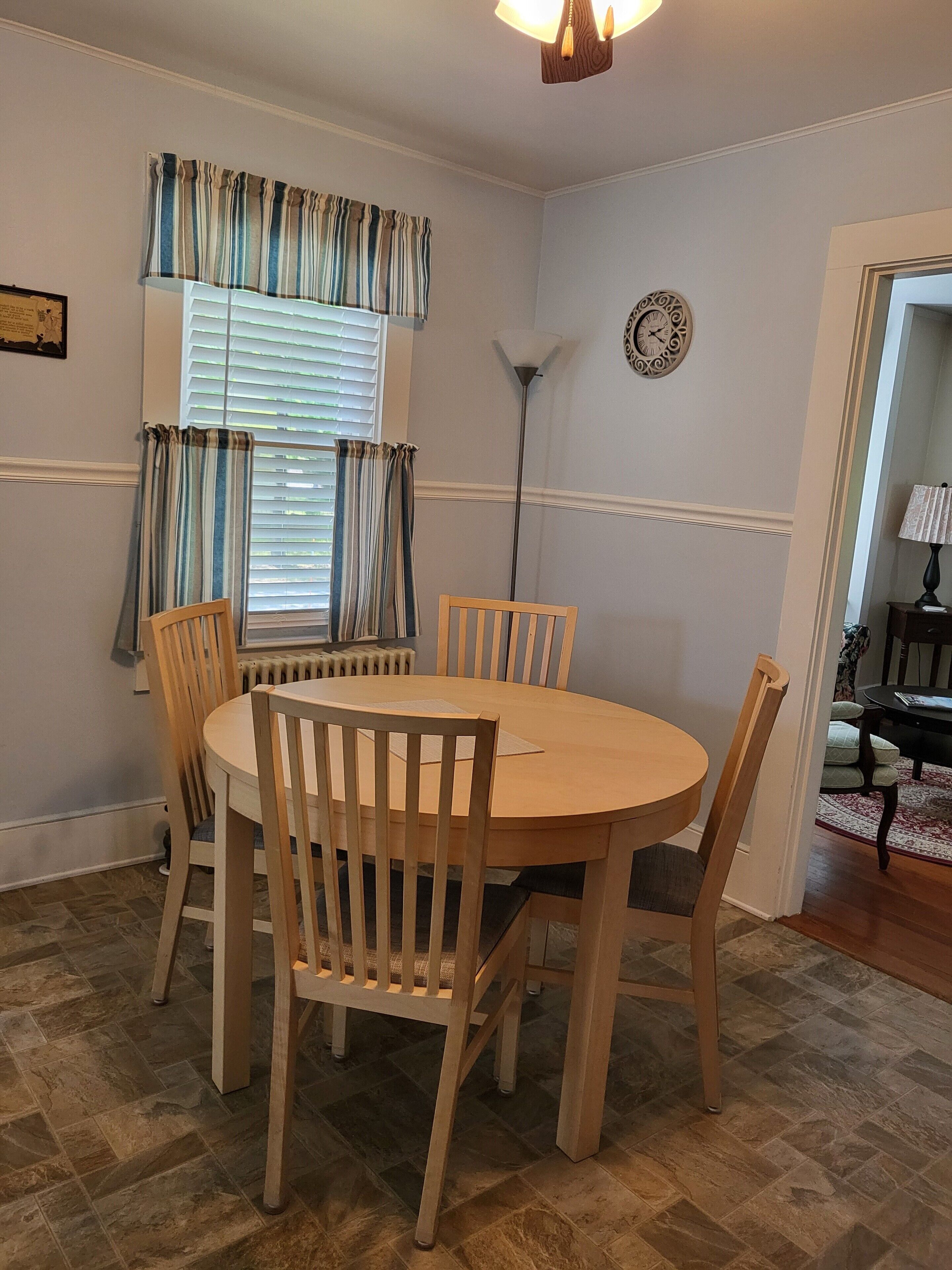 A dining area with a round wooden table and four chairs, a radiator below the window, and a floor lamp.