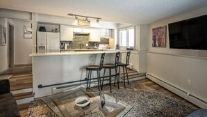 A modern kitchen with a bar area, a dining table with chairs, and a large flat-screen TV mounted on the wall.
