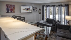 A living room with a marble kitchen island, a grey sofa, and a glass coffee table.